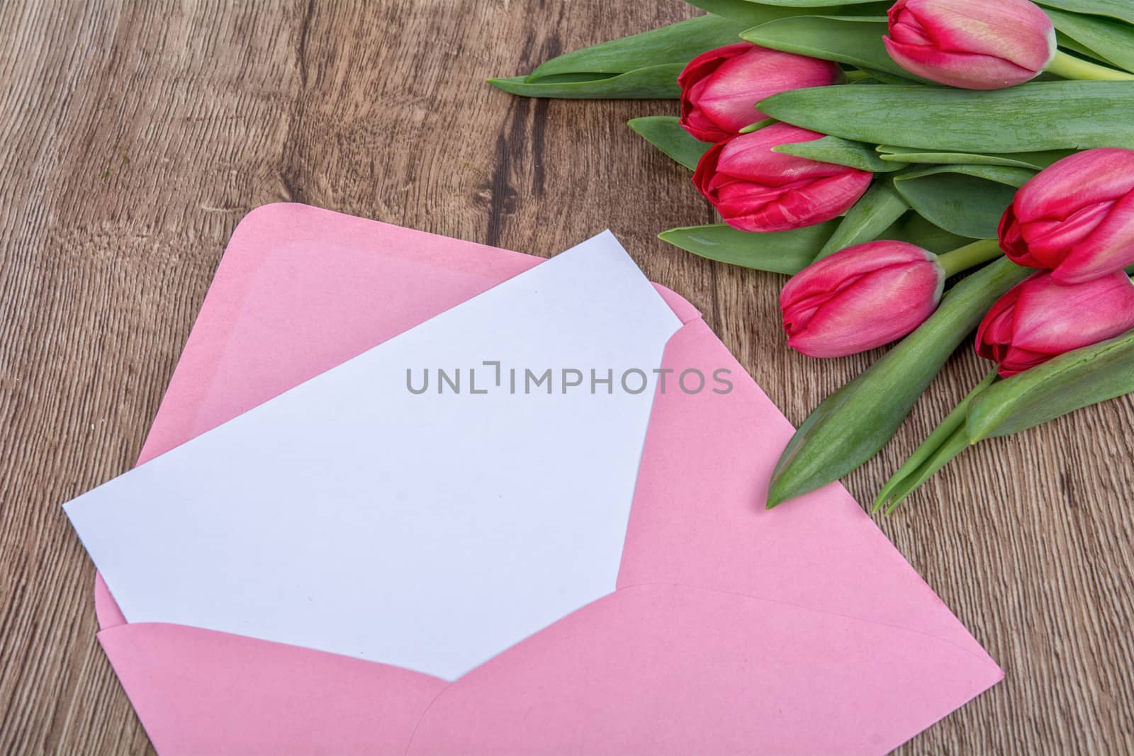 Envelope with sheet of paper and red tulips on a wooden background