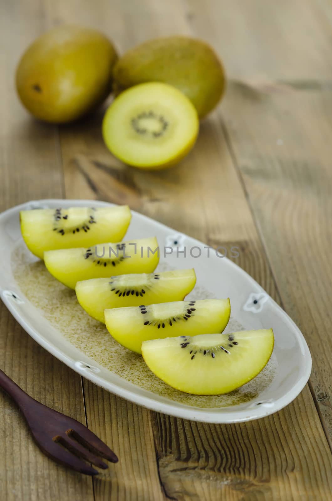 golden kiwi fruit and sliced on dish over wooden background