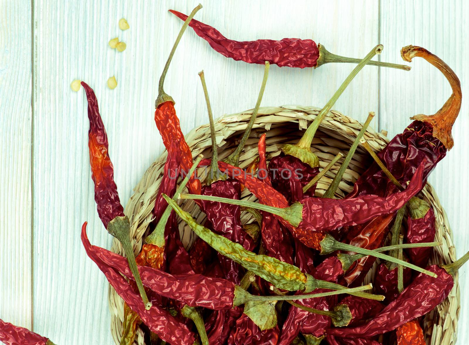 Arrangement of Dried Chili Peppers Full Body with Stems  and Seeds in Wicker Bowl Cross Section on Light Green Wooden background
