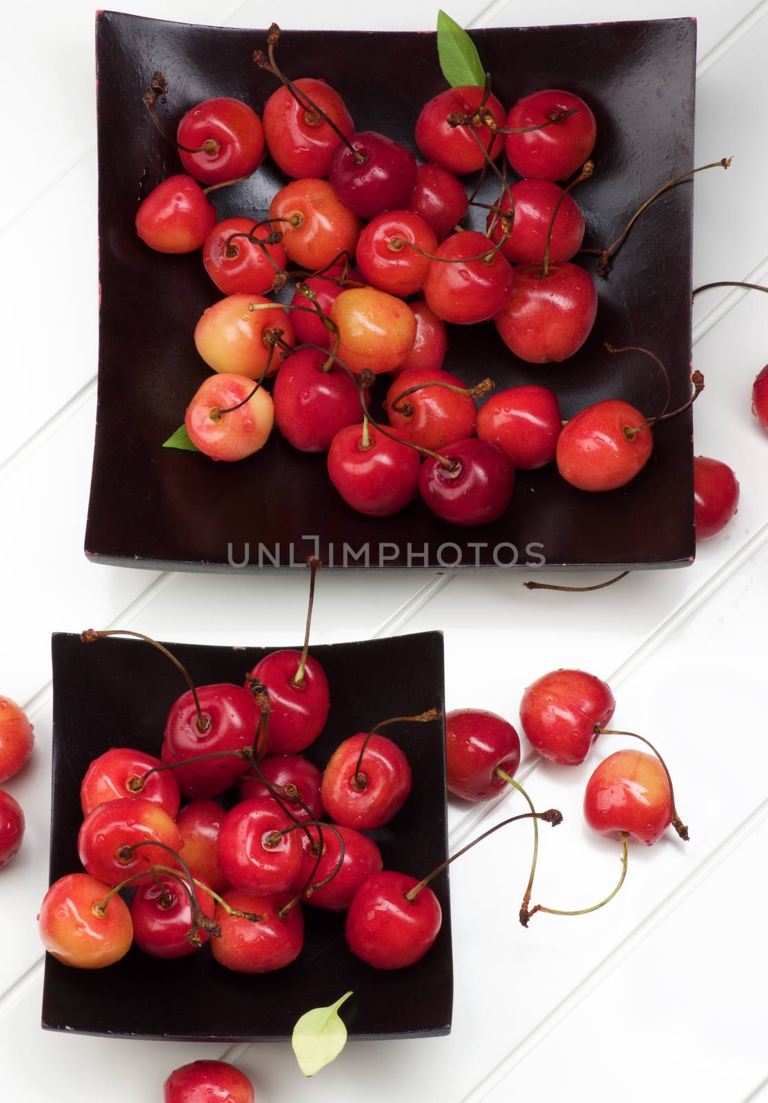 Arrangement of Two Black Plates Full of Fresh Ripe Sweet Maraschino Cherries closeup on Plank White background