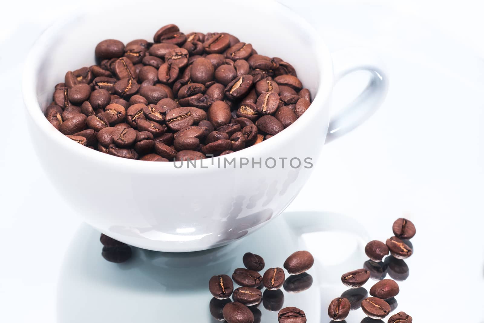 white coffee cupfilled bith coffee beans, with bean on mirror