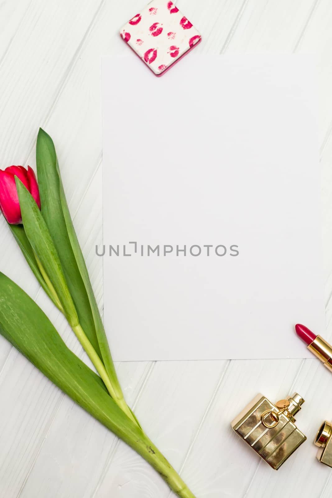 one red tulip, bottle of perfume, lipstick and sheet of paper for your greetings on the background of white wooden board