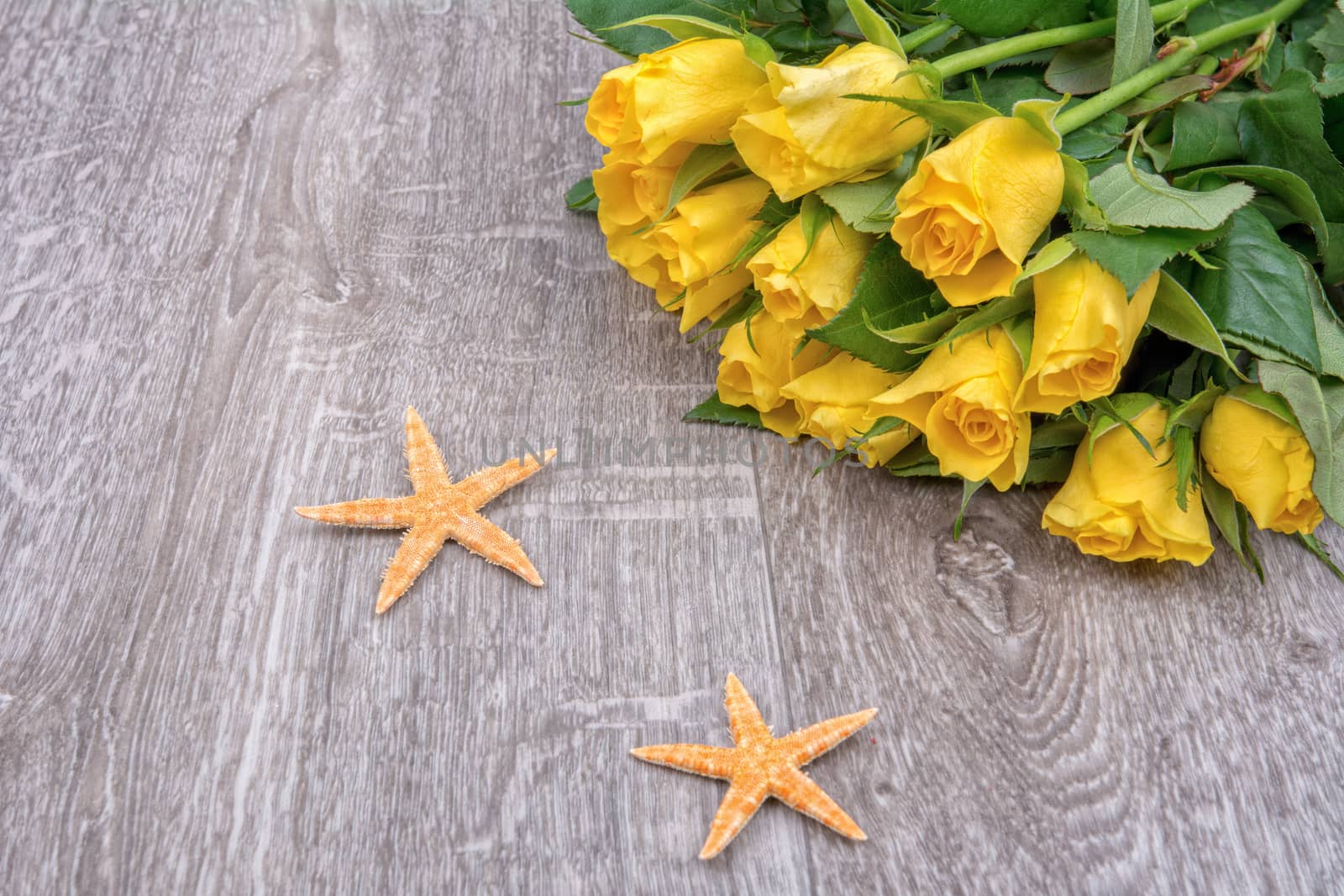 Orange starfishes and yellow roses on a wooden background