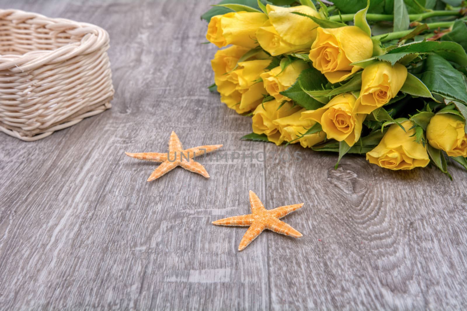 Orange starfishes and yellow roses on a wooden background