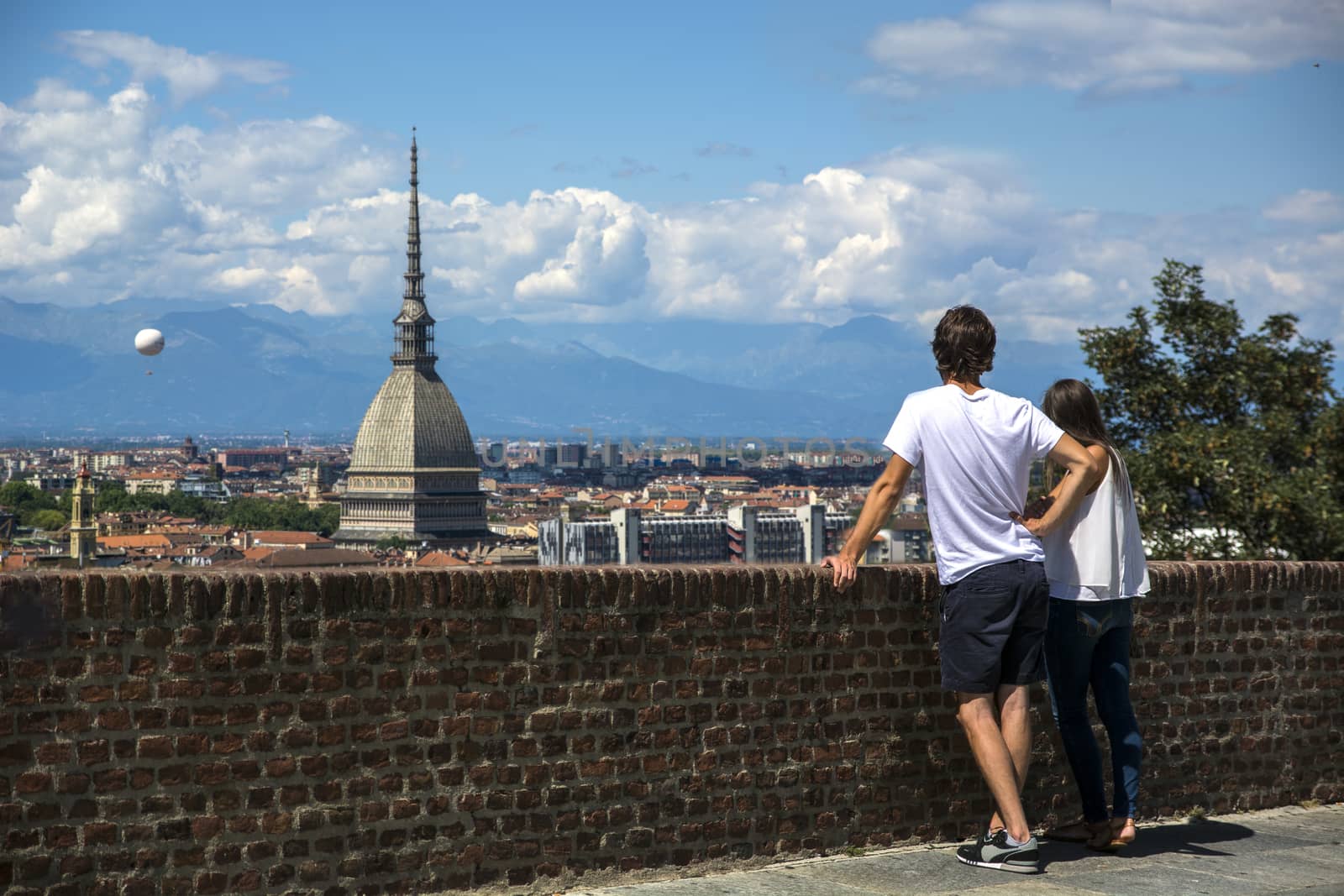 Panoramic view of Turin city center, in Italy, with couple admiring the view in a sunny day, with Mole Antonelliana and Alps in the background