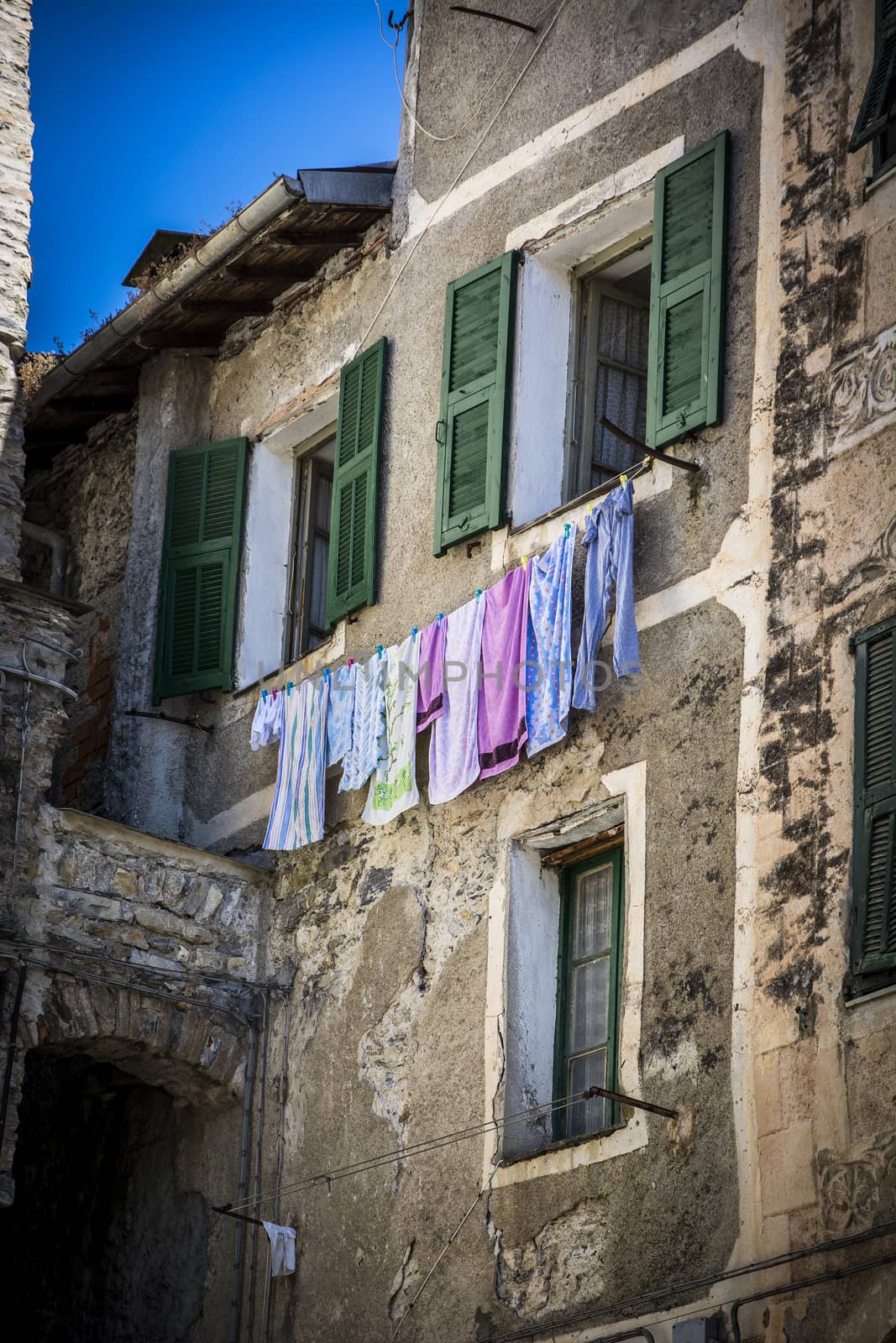 Old rough stone building with colorful windows and clothing on string in small Italian town.