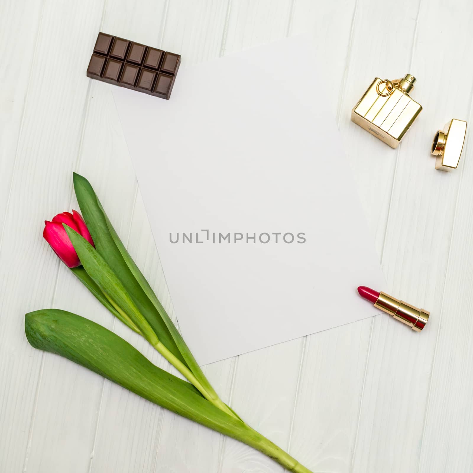 top view beautiful one red tulip, necklace, lipstick, piece of chocolate and sheet of paper for your greetings on the background of white wooden board