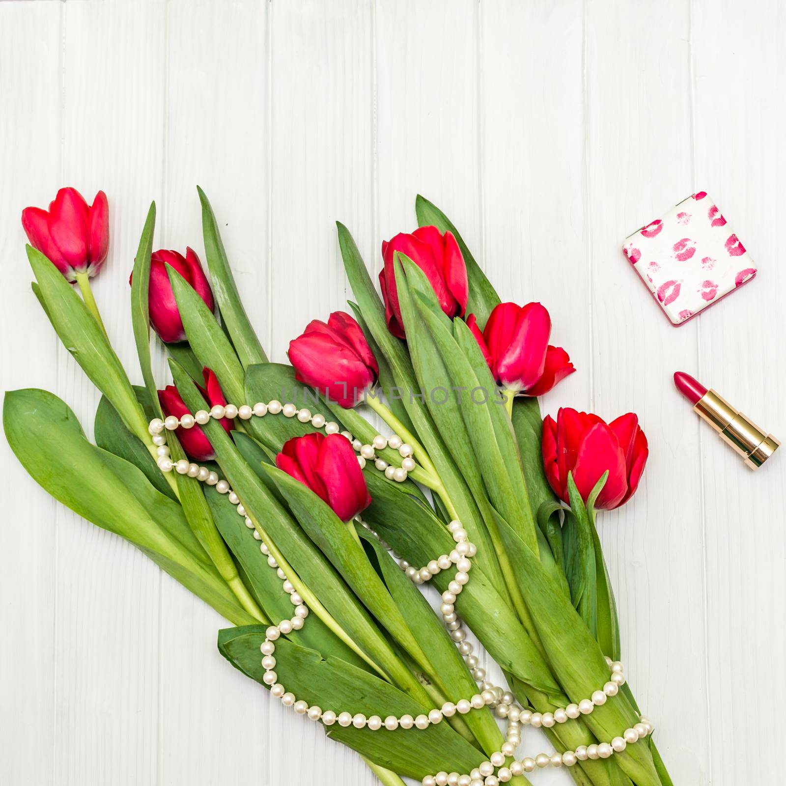 top view beautiful bouquet of red tulips in the necklace, lipstick on the background of white wooden board