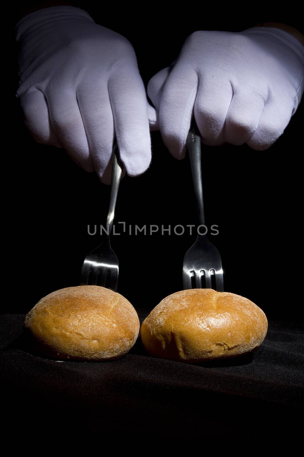 Buns on the forks and hands in white gloves on a black background
