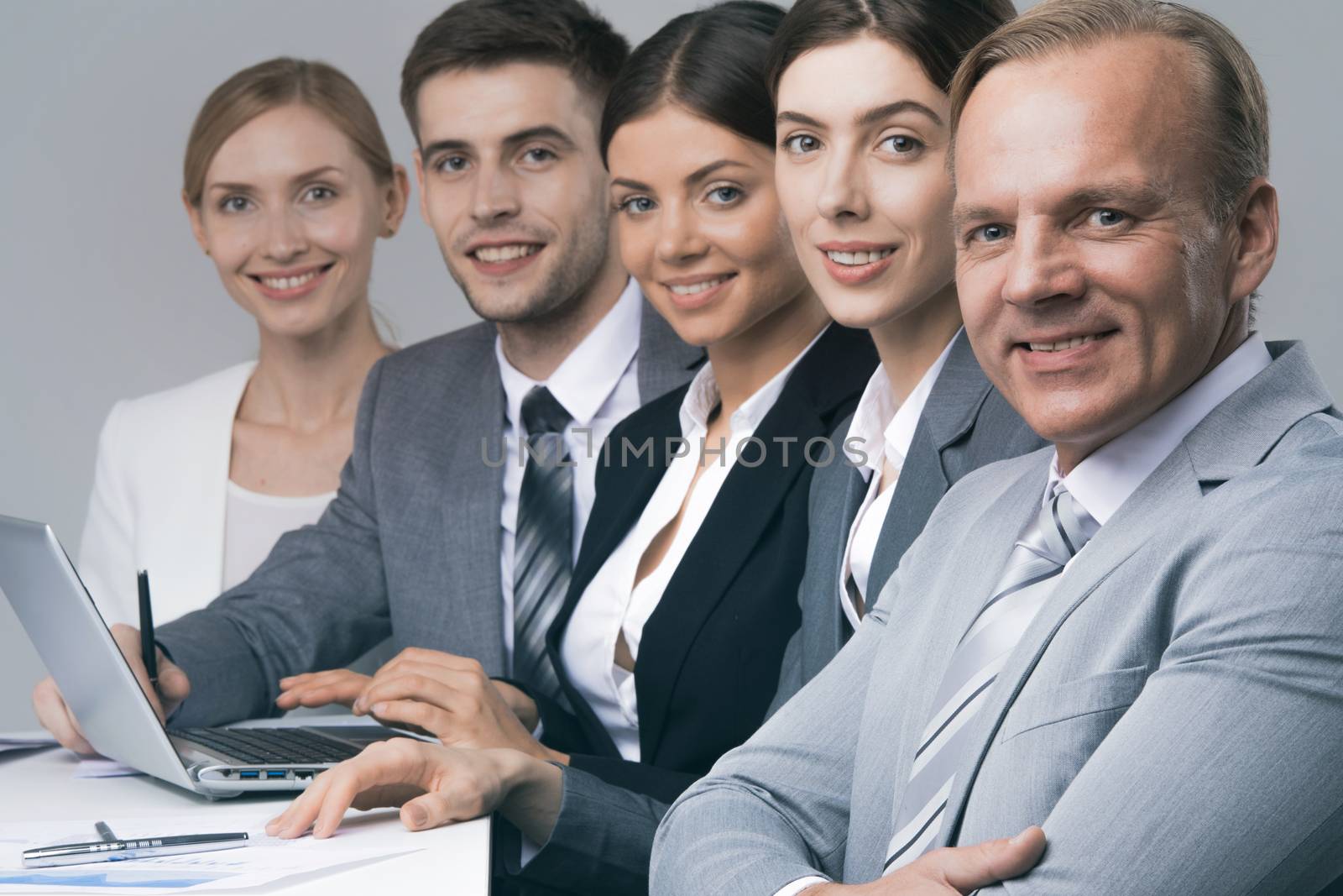 Smiling business people sitting in a row and working at the table with laptop