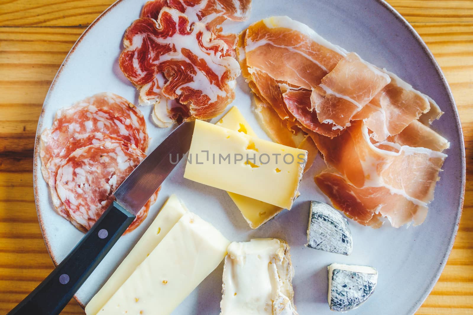 Plate with a variety of Italian cheese and charcuterie, on a wooden table