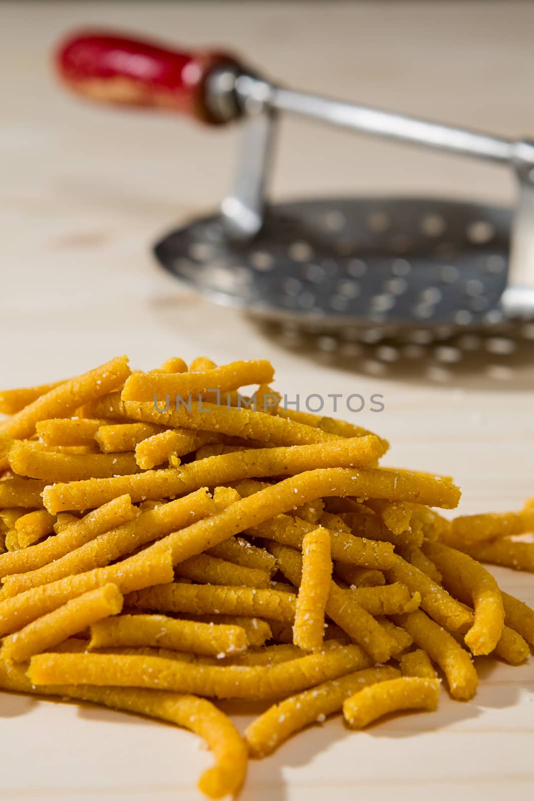 Closeup of Passatelli original Italian pasta over a wooden background and its tool