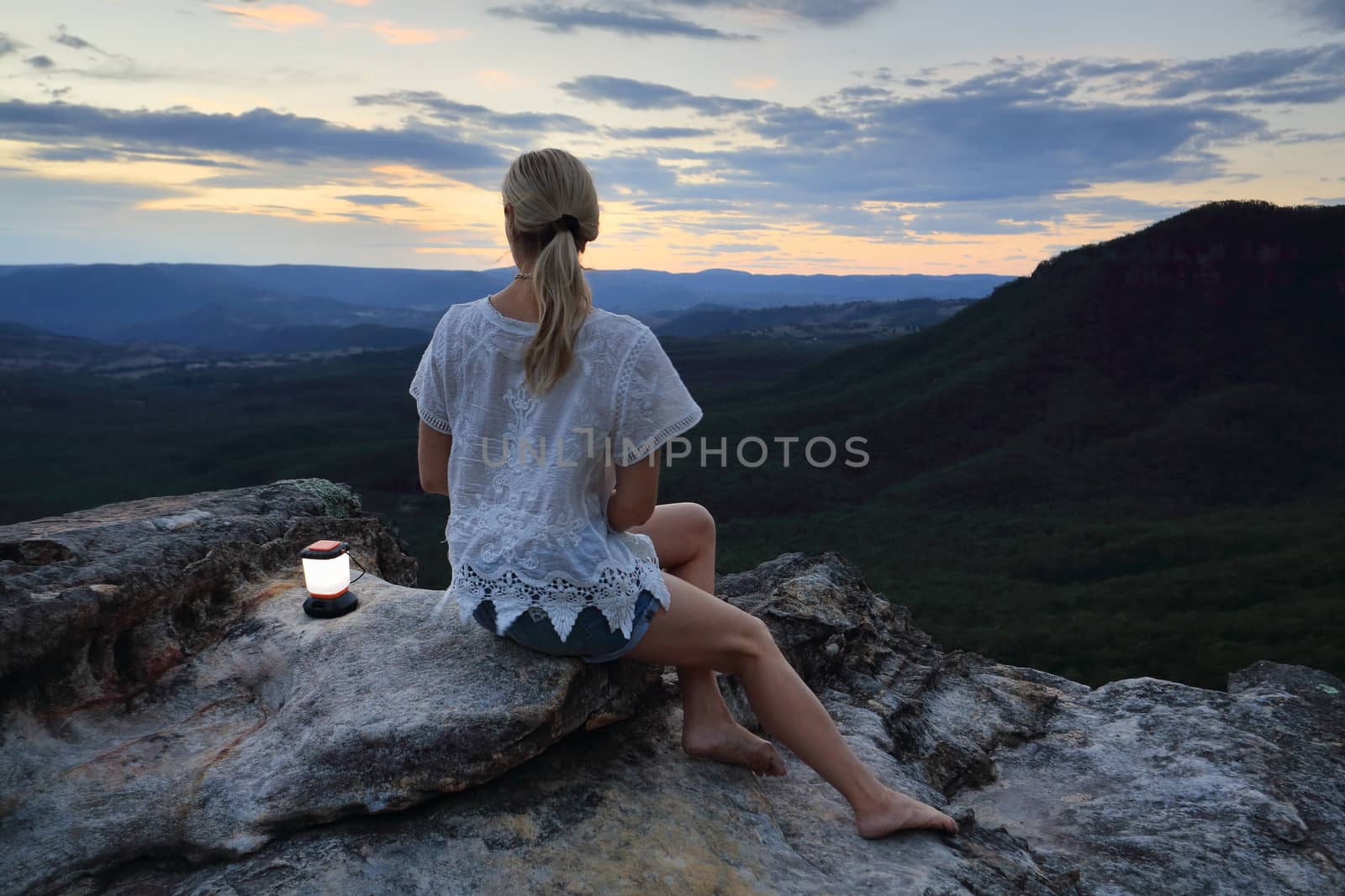 Woman relaxing perched on a rocky outcrop with views high up in the mountains to the valley below and beyond.

Location:  narrowneck, Blue Mountains, Australia,