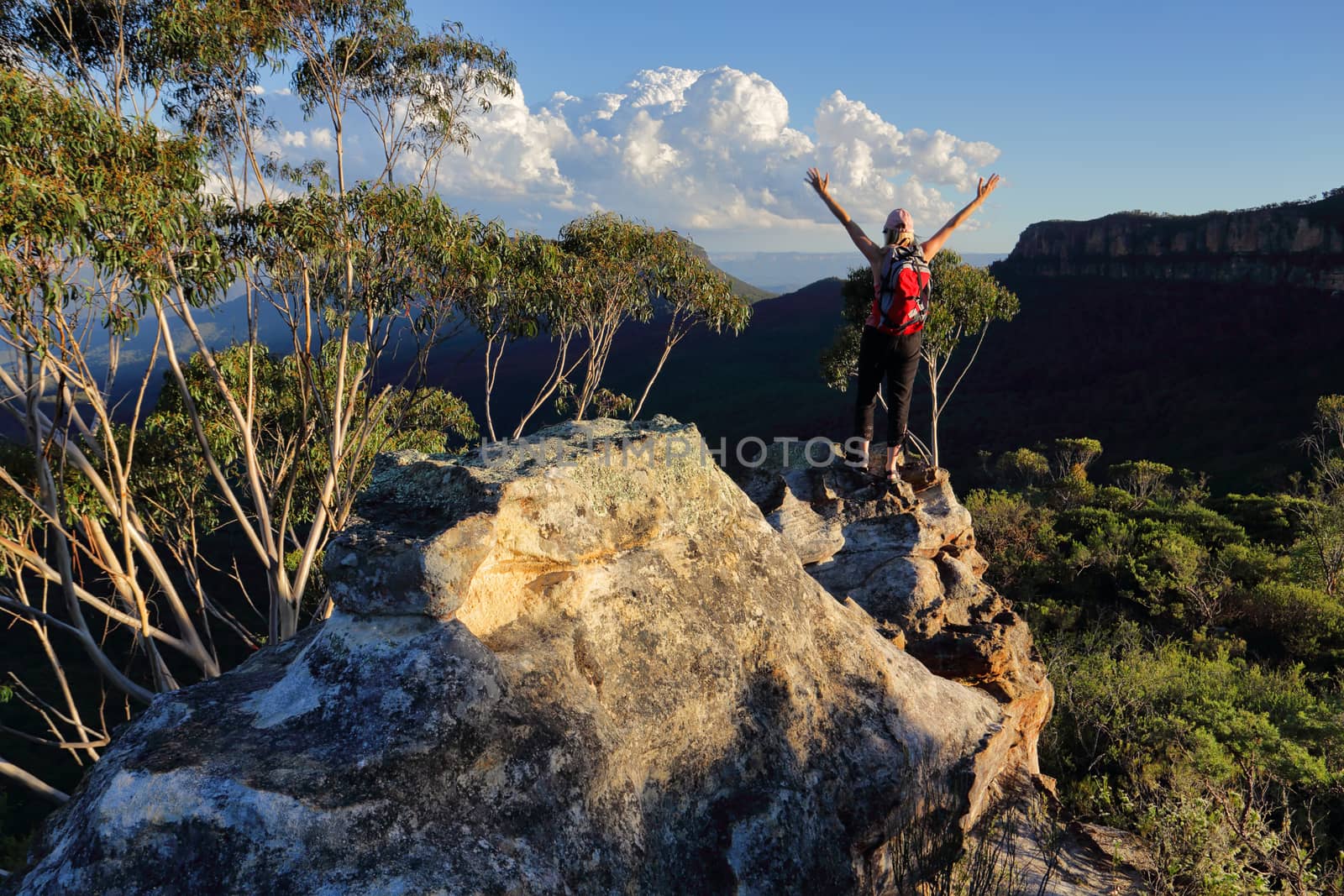 Woman with feeling of exhilaration, standing on top of mountain arms outstretched, with views over the valley and other mountains landscape
