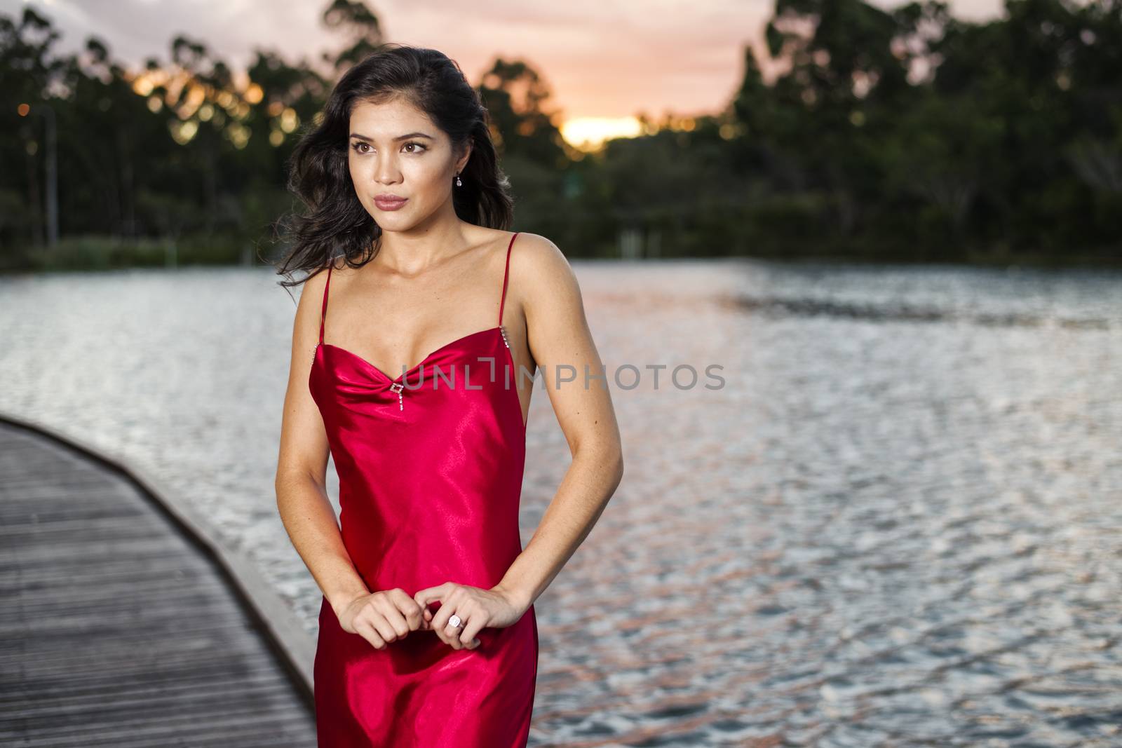 Beautiful young woman wearing a long red silk formal dress in the gardens in the afternoon.