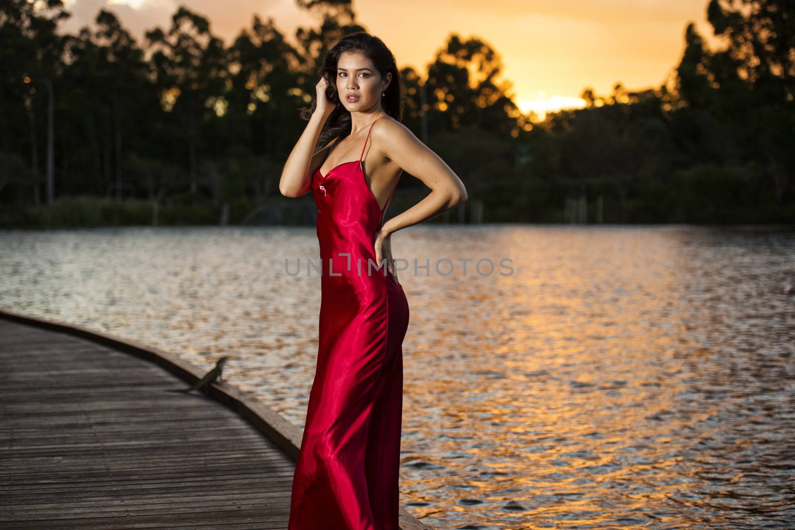 Beautiful young woman wearing a long red silk formal dress in the gardens in the afternoon.