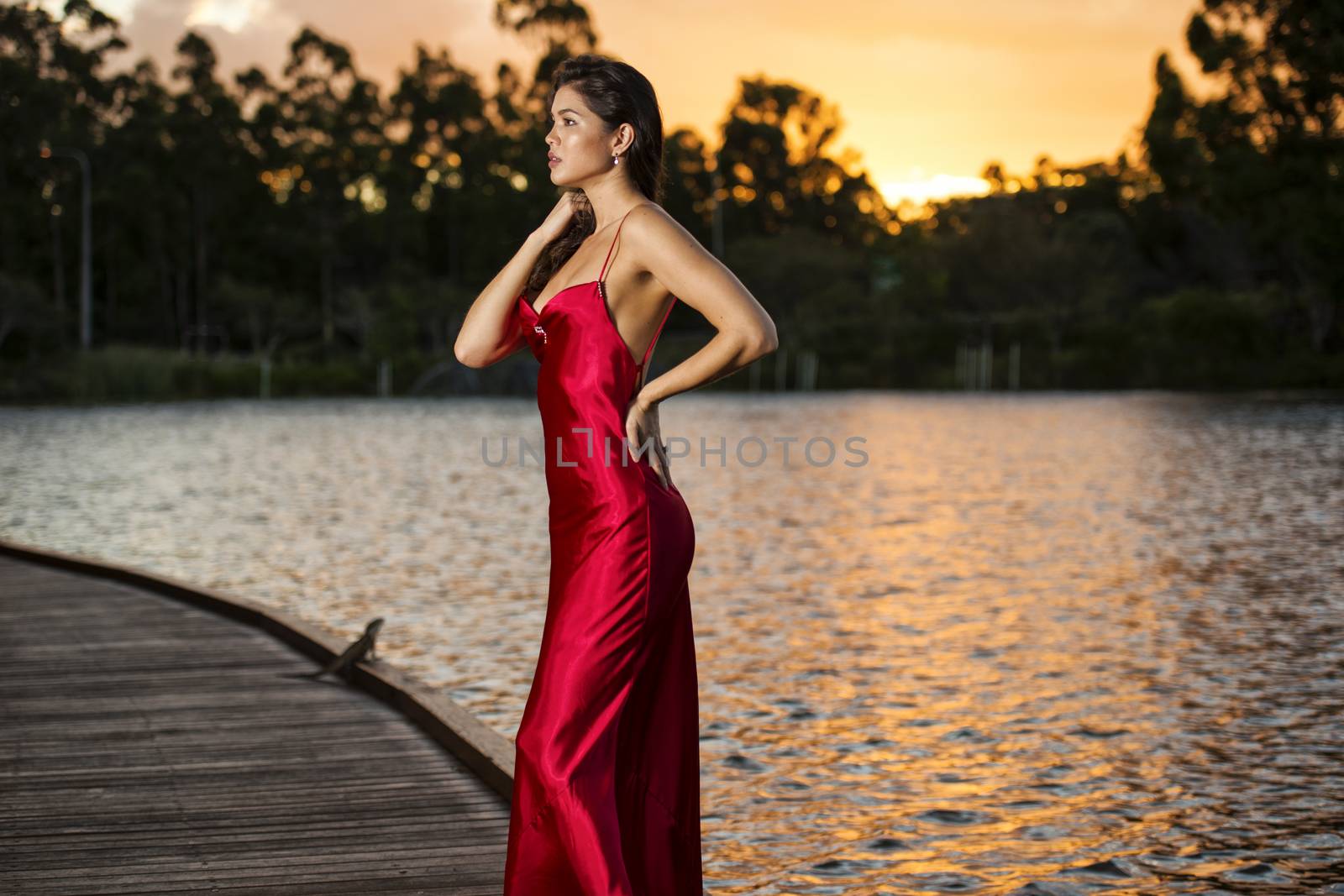 Beautiful young woman wearing a long red silk formal dress in the gardens in the afternoon.