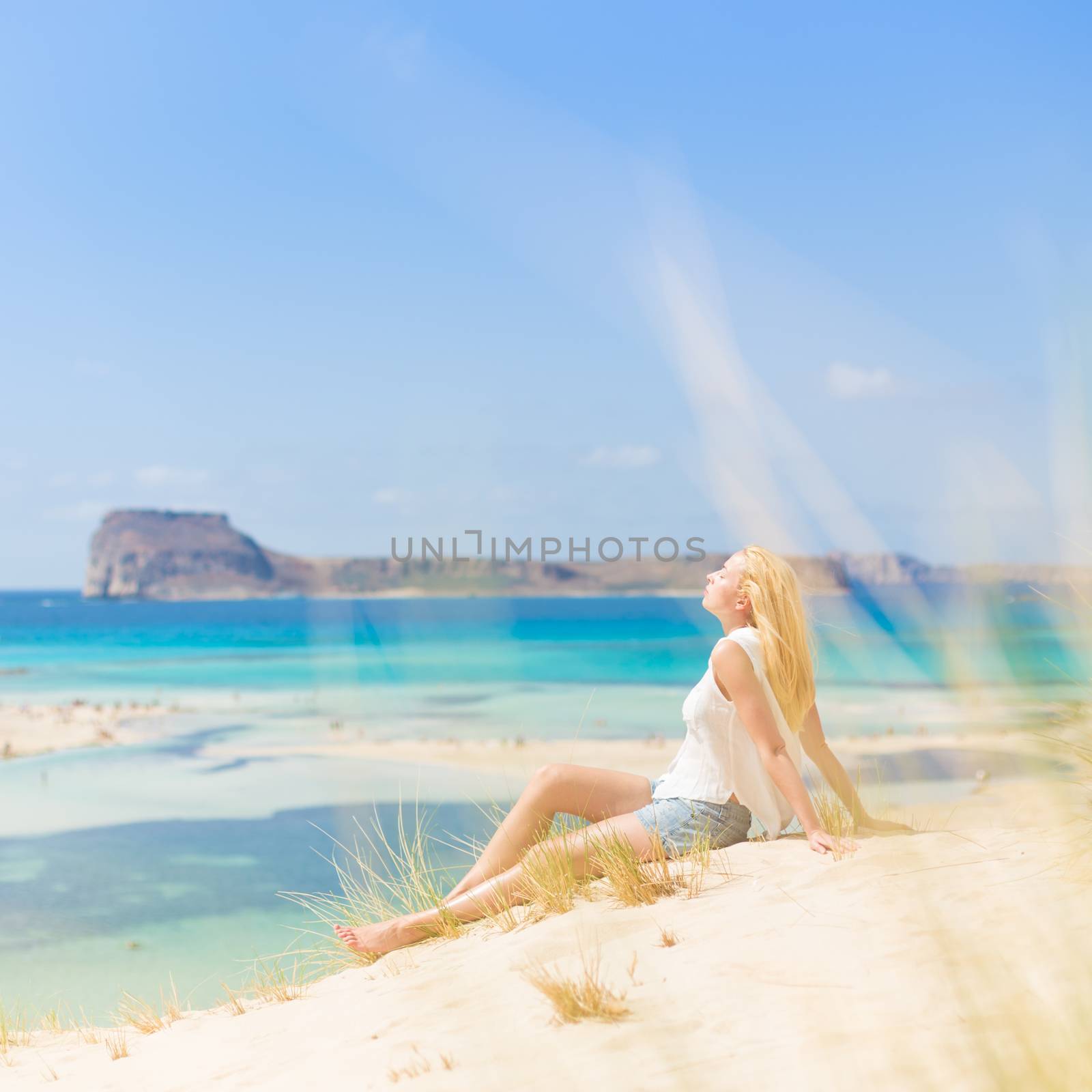 Relaxed woman enjoying sun, freedom and life an a beautiful sandy beach of Balos in Greece. Young lady feeling free, relaxed and happy. Vacations, freedom, happiness, enjoyment and well being.