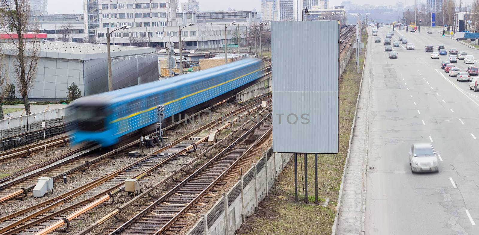 Train of a metro system moving on the overground part of the subway line and city street with moving cars beside 
