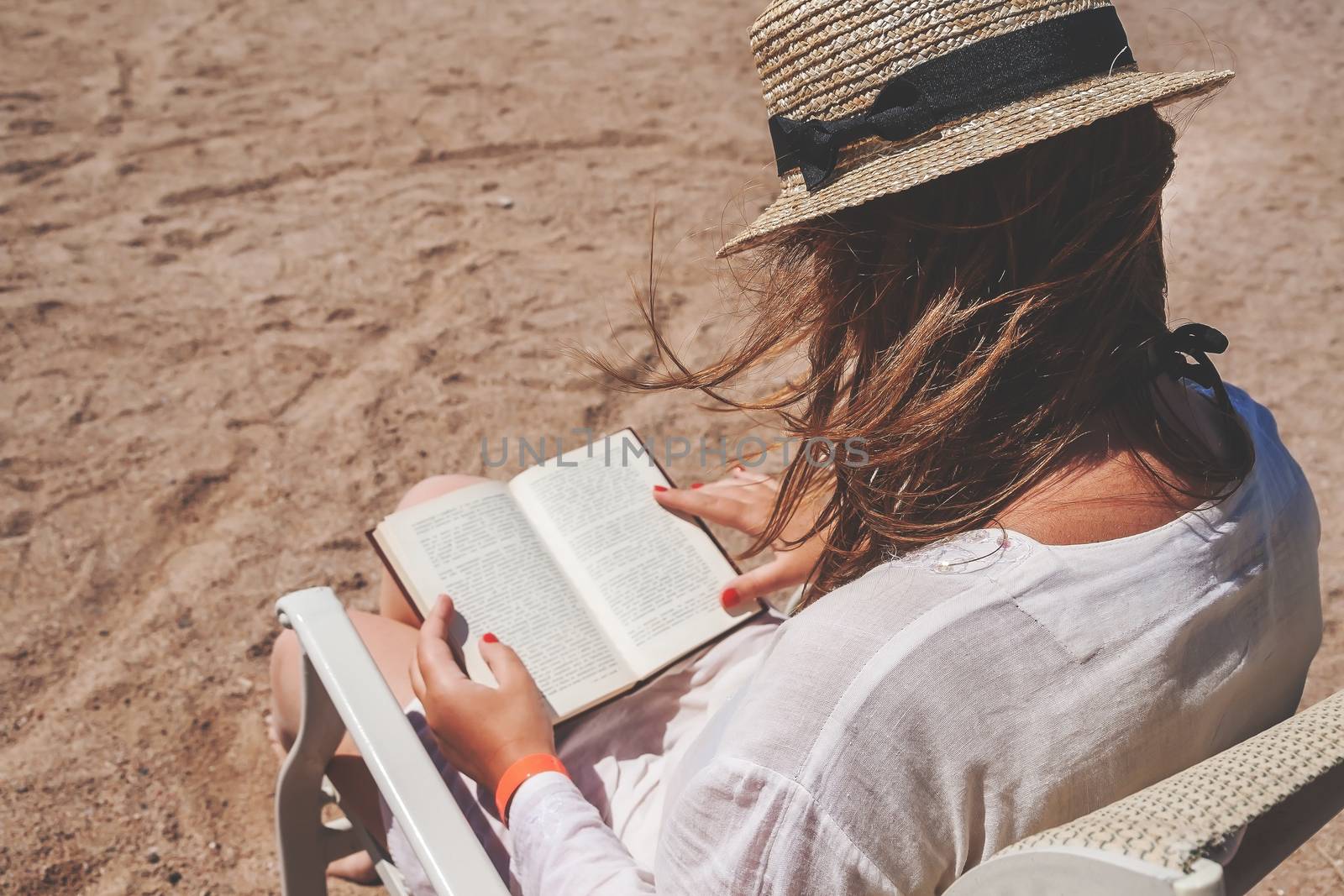 Young adult woman with a hat on the beach reading a book by Tanacha