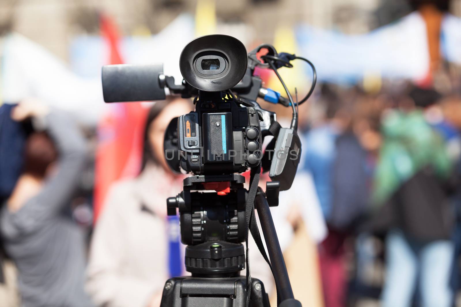 Filming female journalist with a television camera, blurred people in the background. Television broadcasting.