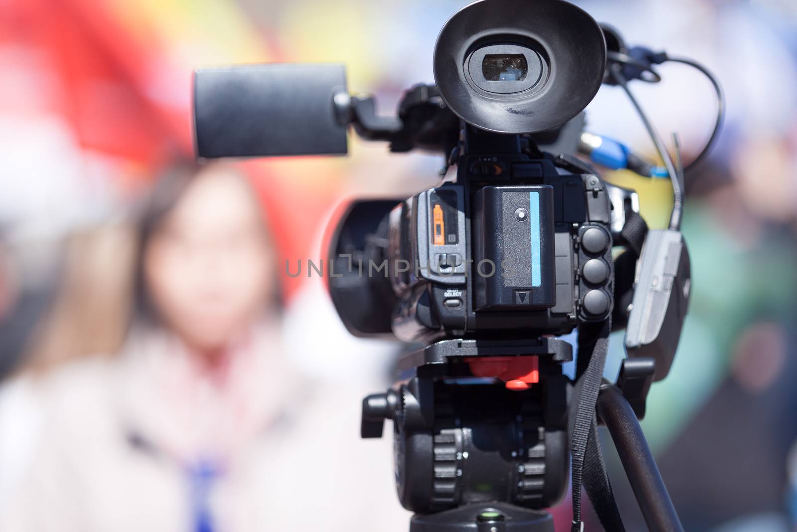 Television camera in the focus, blurred female journalist in the background. TV broadcasting.
