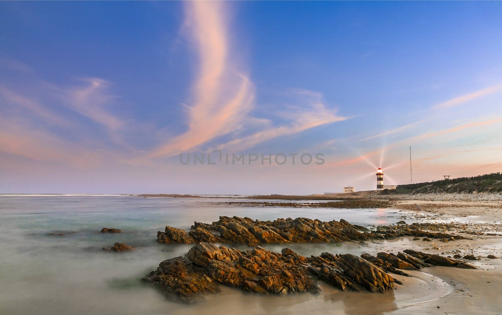 Lighthouse at dusk with rocks in the foreground by fouroaks