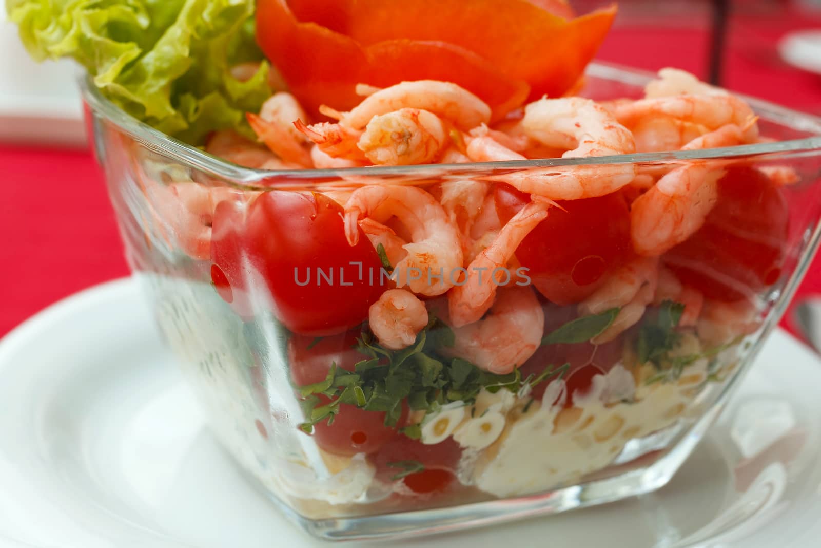 Seafood salad with shrimps and fresh vegetables, on a serving table. On a red tablecloth close-up