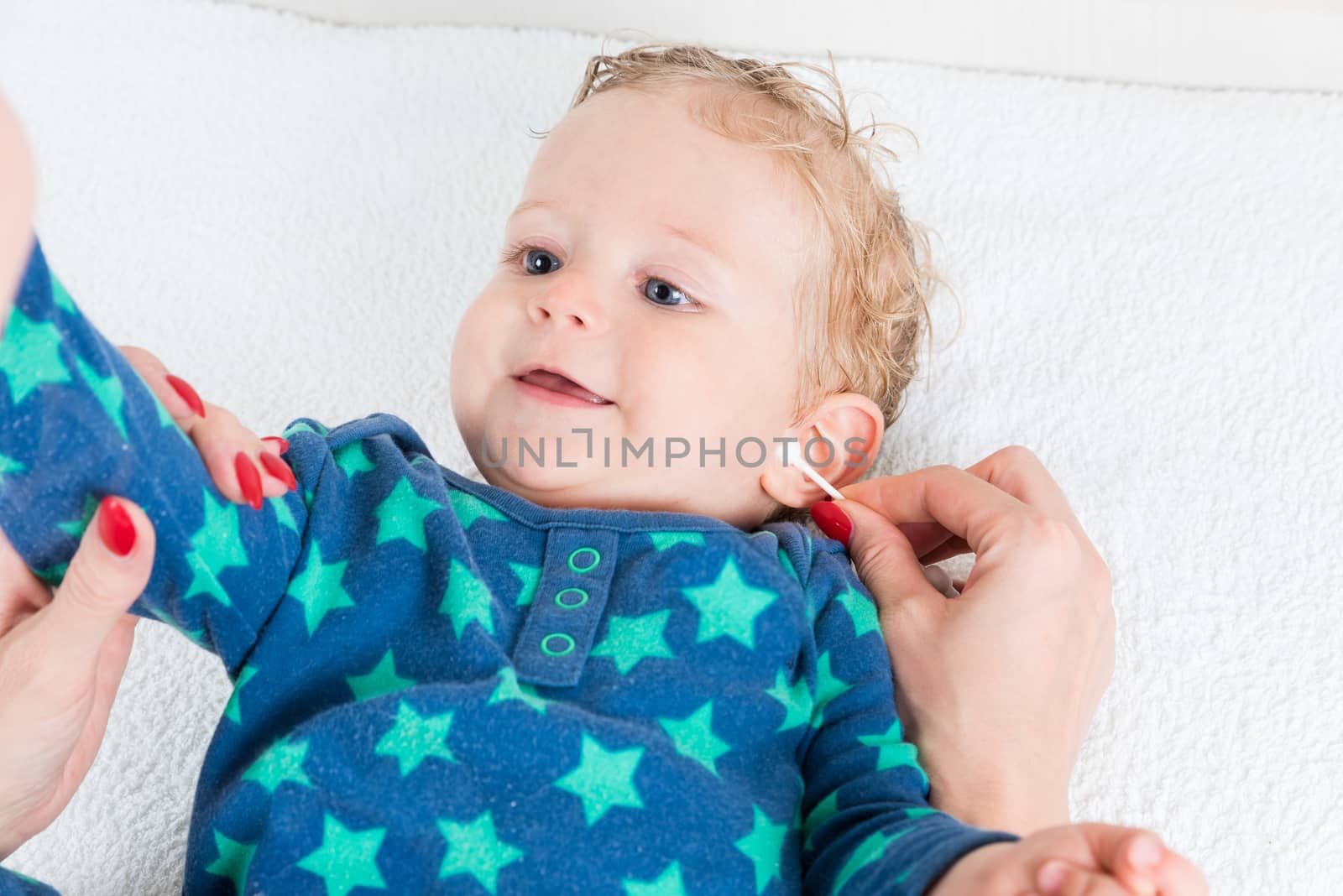 Mother hand cleaning baby ear with cotton swab,infant lying with wet hair and blue eyes,copy space,horizontal photo.