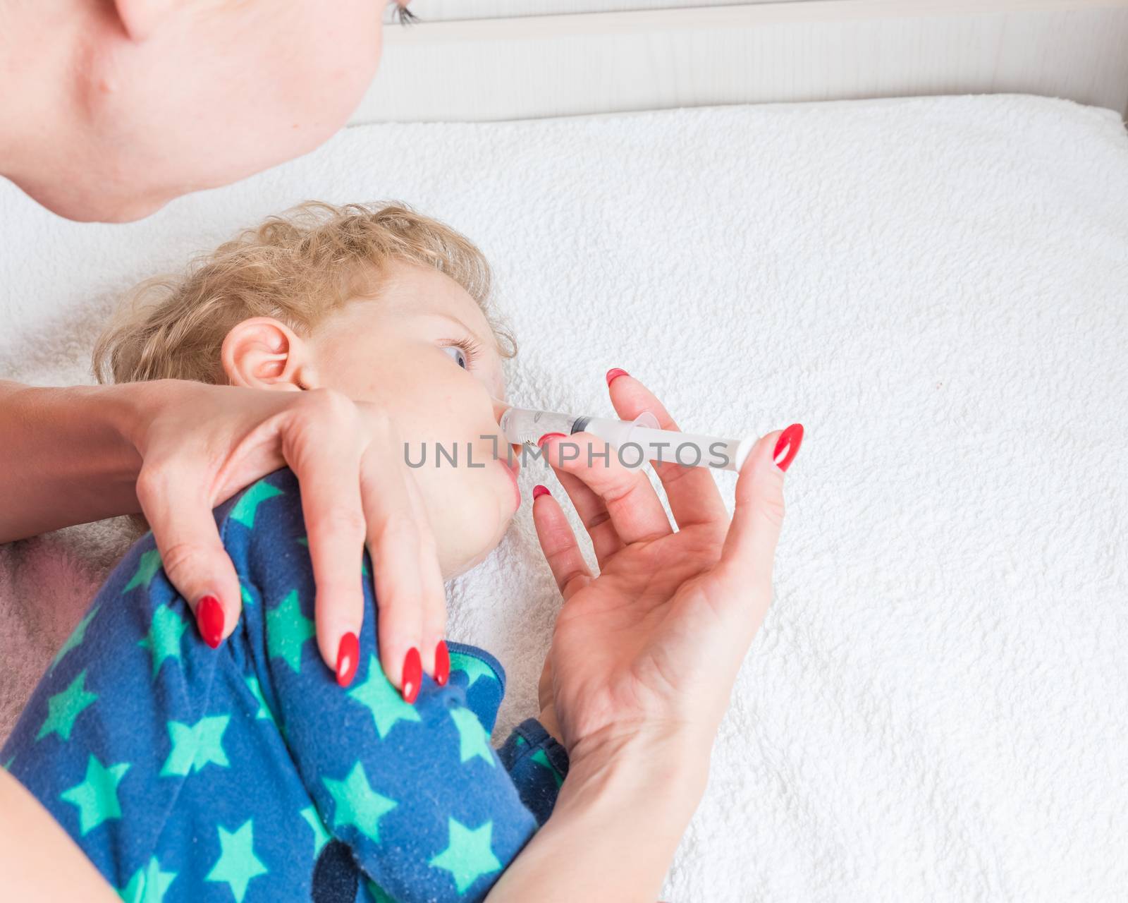 Mother cleans the baby's nose with a syringe with saline water, while the infant is lying.