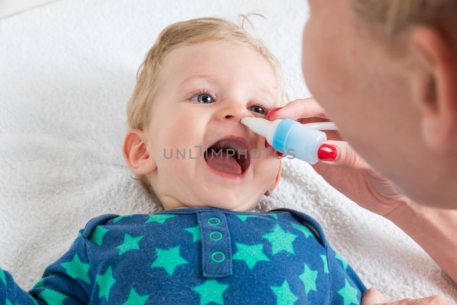 Mother cleans the baby's nose with a blower, while the infant is lying and smiling.