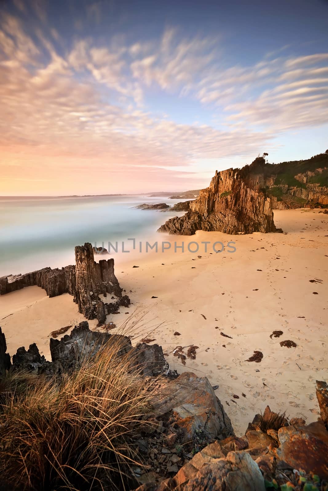 Early morning hues standing high on a sea stack and views south across the beach and sea stacks of Mullimburra Point South beach in Eurobodalla National Park.  Long Exposure.