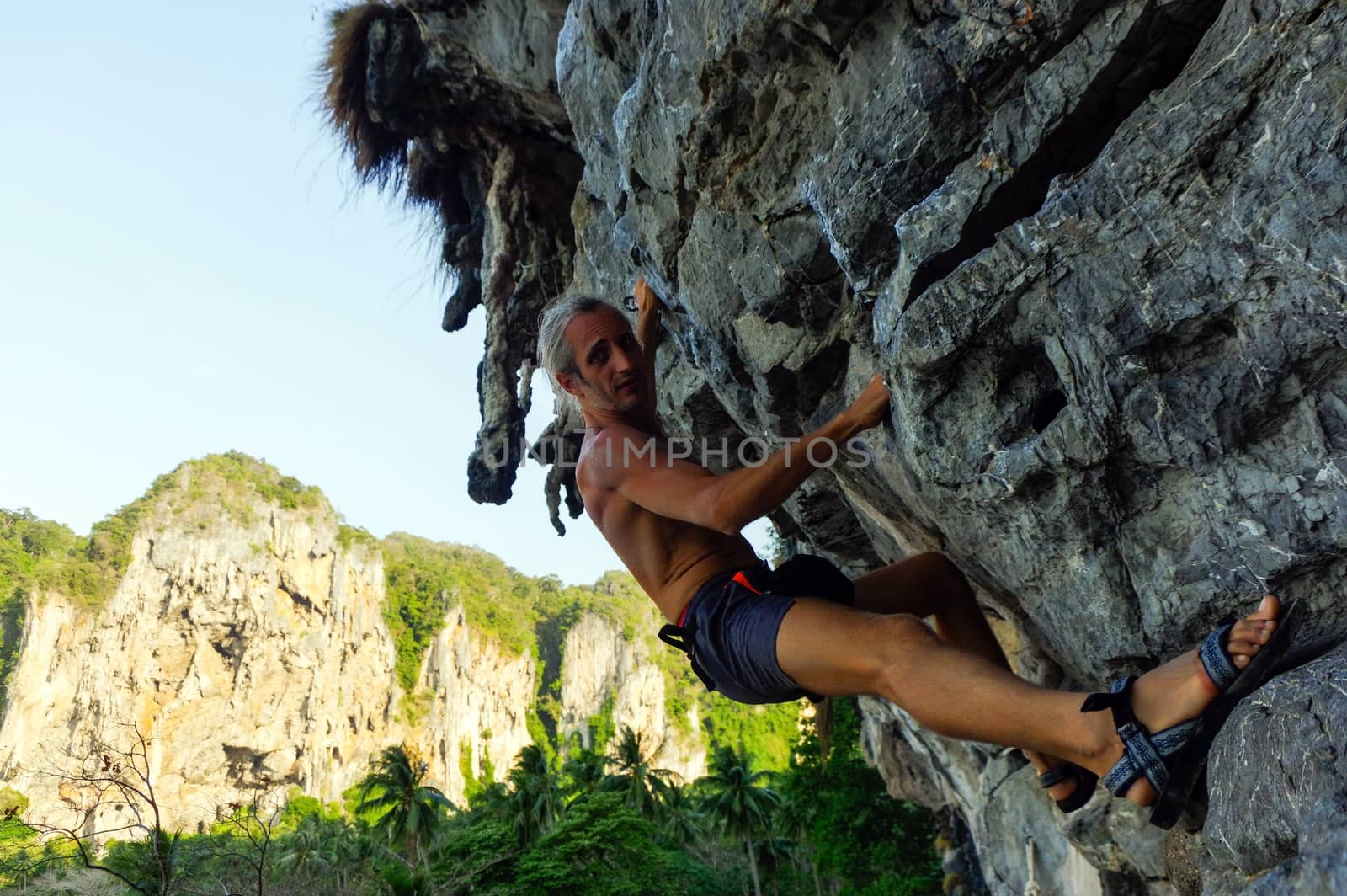 a strong and happy man climbing on high rock over the sea with a hut. Tonsai beach in Thailand by evolutionnow