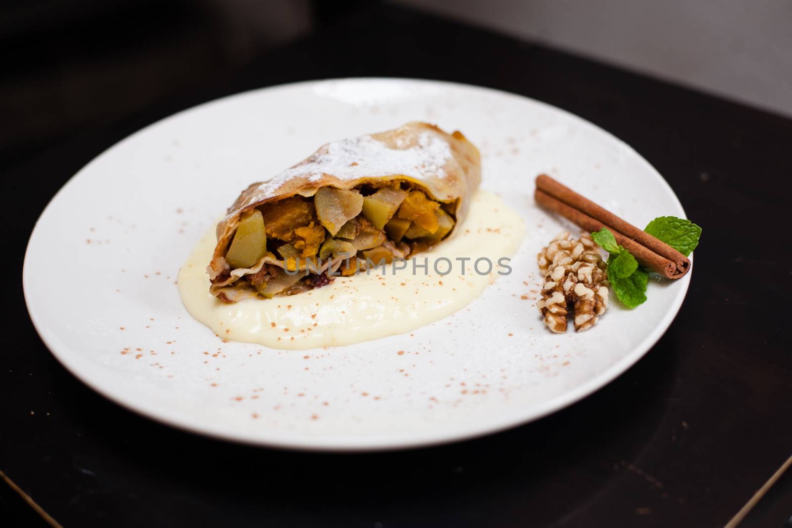 A piece of apetite strudel with orange, nut, cinnamon pod on a white plate