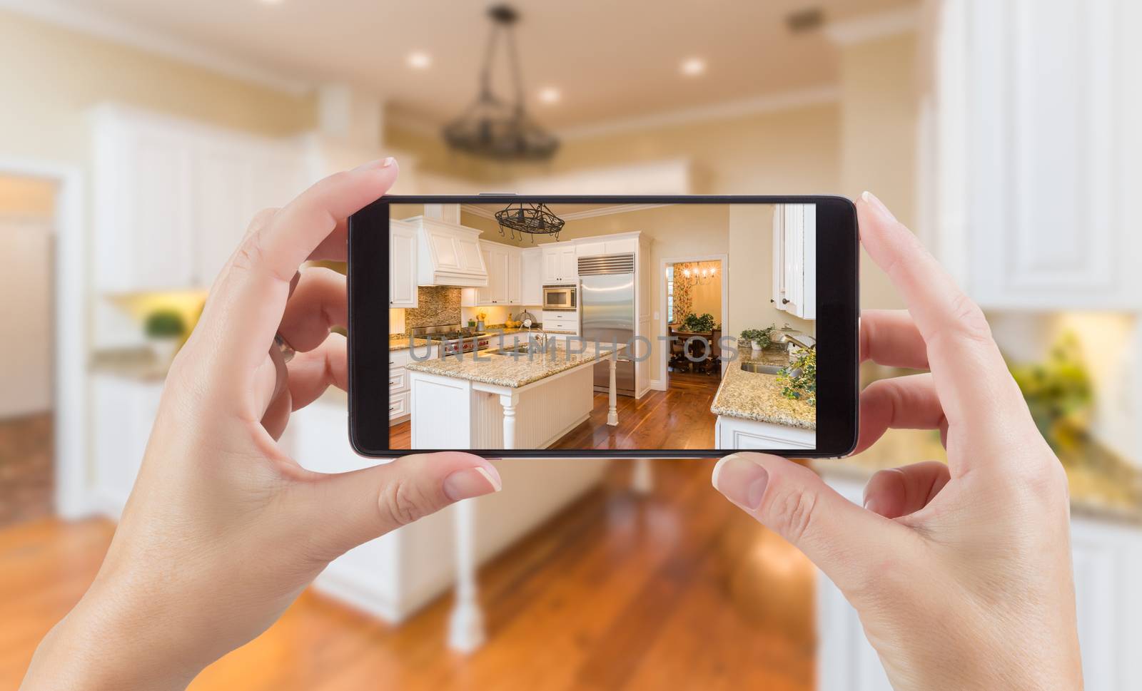 Female Hands Holding Smart Phone Displaying Photo of Kitchen Behind. by Feverpitched