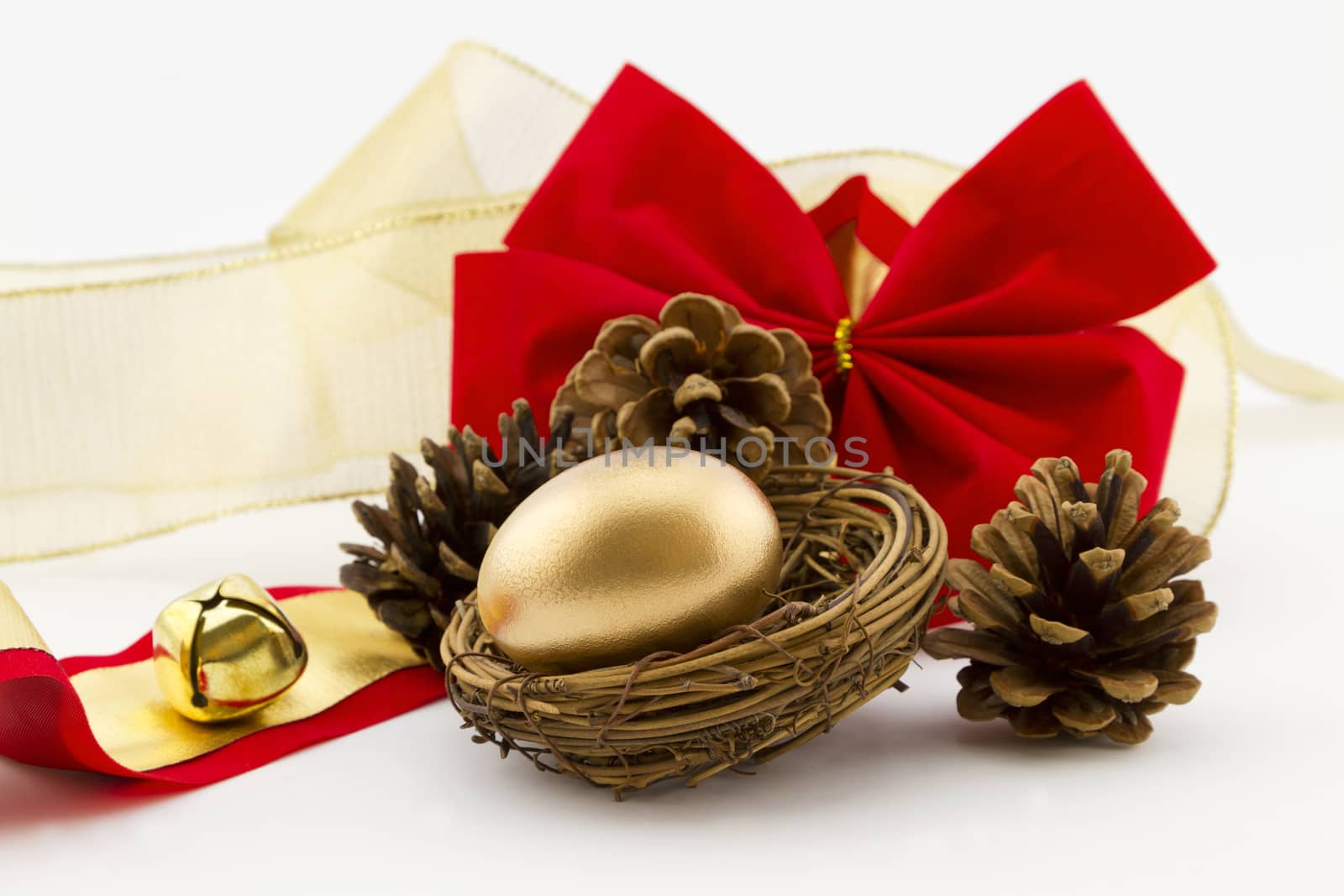 Gold nest egg surrounded by pine cones placed with red velvet bow and gold bell and ribbon.  Holiday financial gift is festive.  
