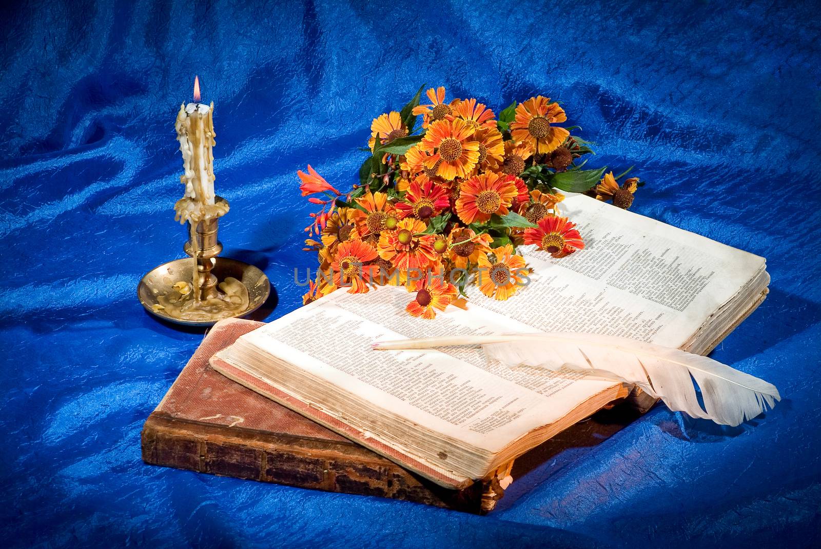 Candle, books and goose feather on fabric background