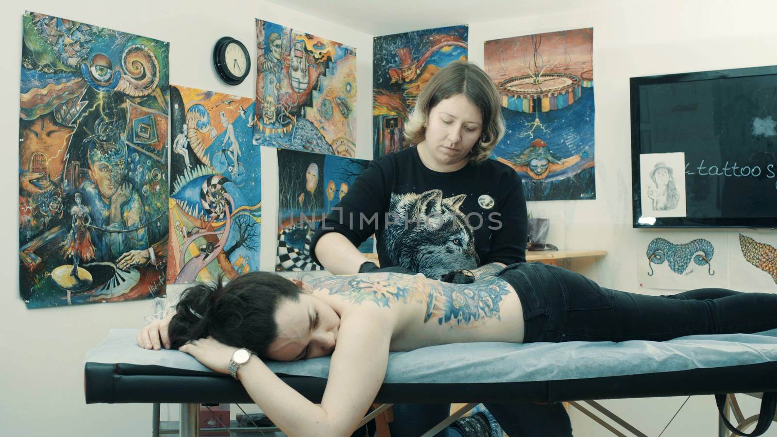 Master tattooist holding a tattoo machine making a tattoo on the girl's back.