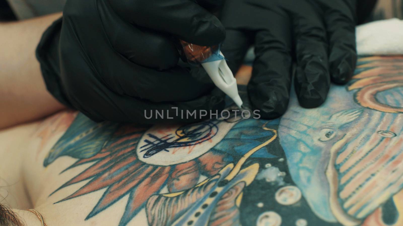 Tattooist making a tattoo on the girl's back by Chudakov