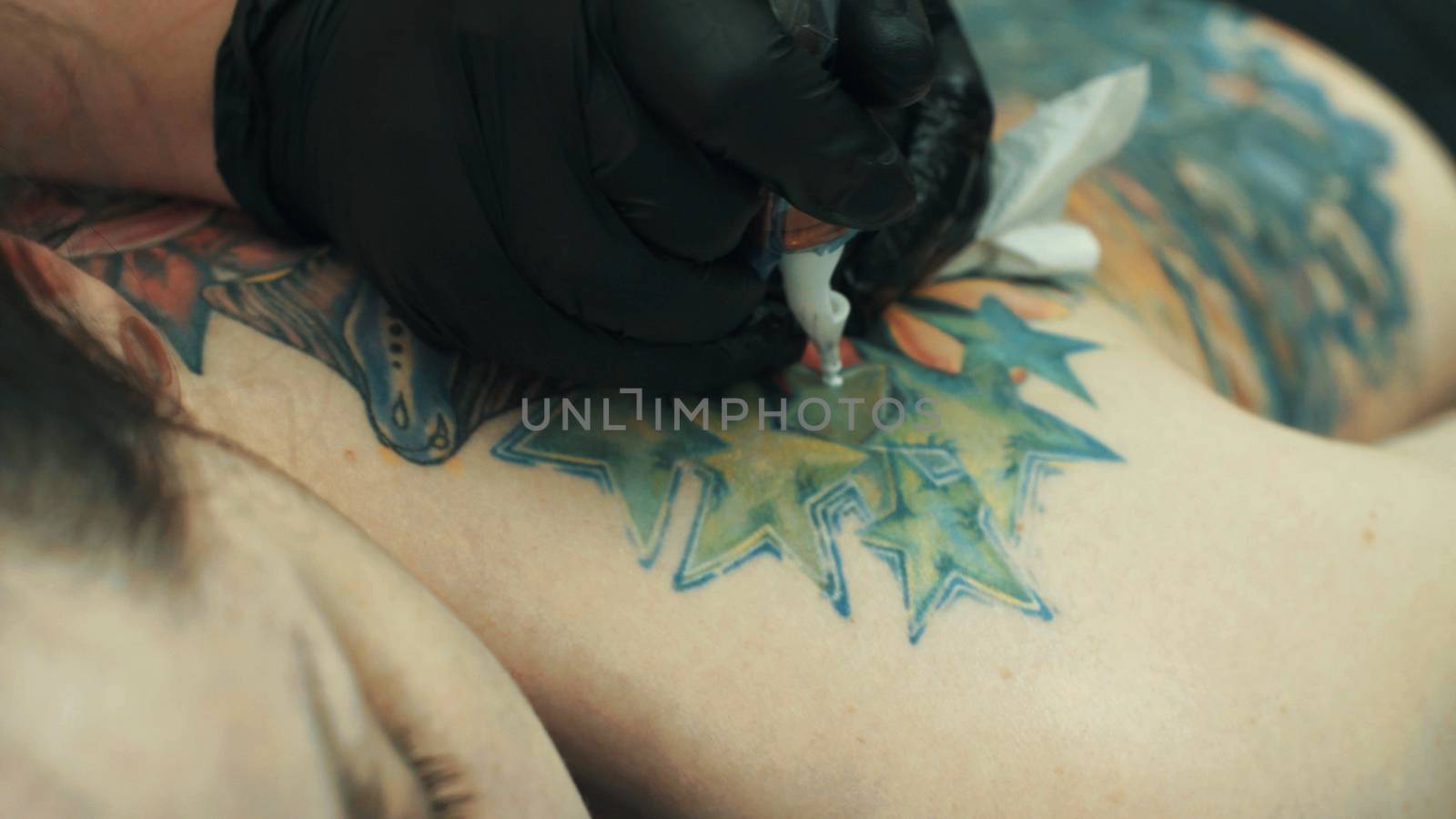 Master tattooist holding a tattoo machine making a tattoo on the girl's back. Close up