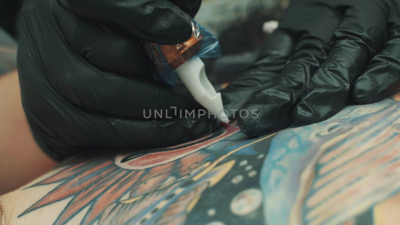Master tattooist holding a tattoo machine making a tattoo on the girl's back. Close up