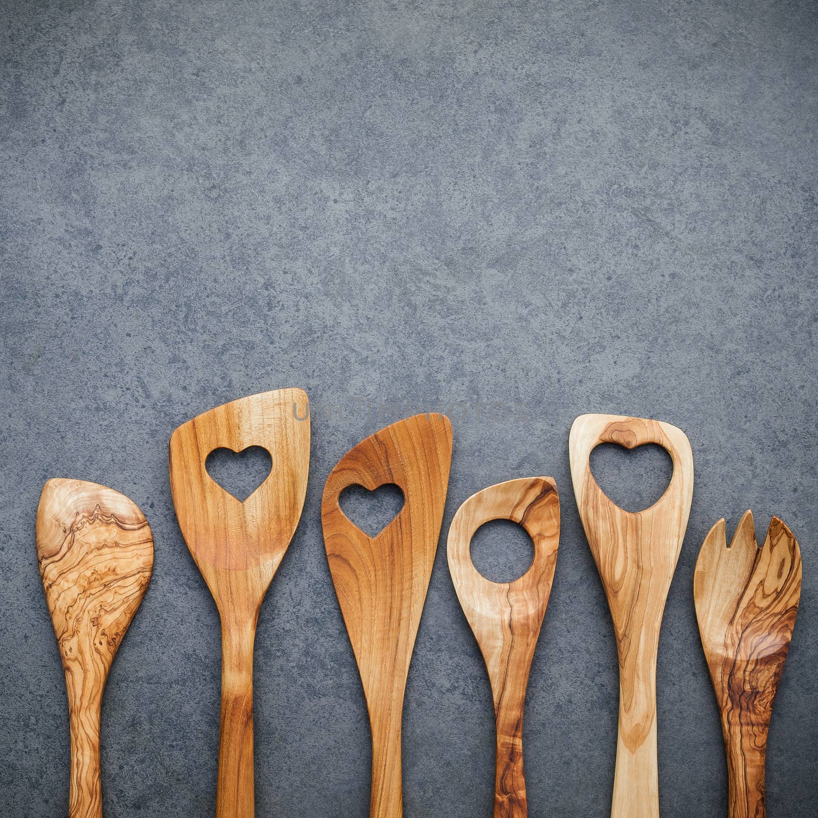 Various wooden cooking utensils border. Wooden spoons and wooden spatula on dark stone background with flat lay and copy space.