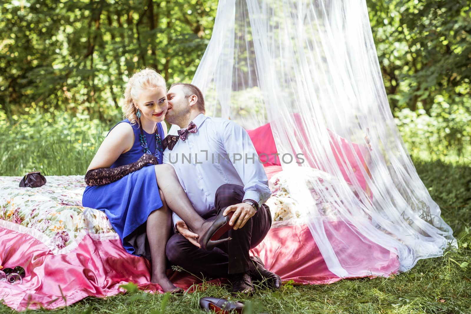 Man and woman sitting on the bed in the lawn and man takes off shoes from women in Lviv, Ukraine.