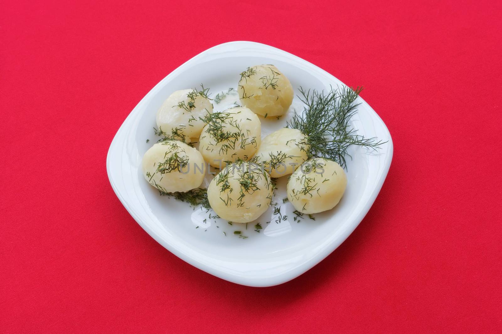 Boiled potatoes with herbs on a plate and red tablecloth. Close-up view from above.