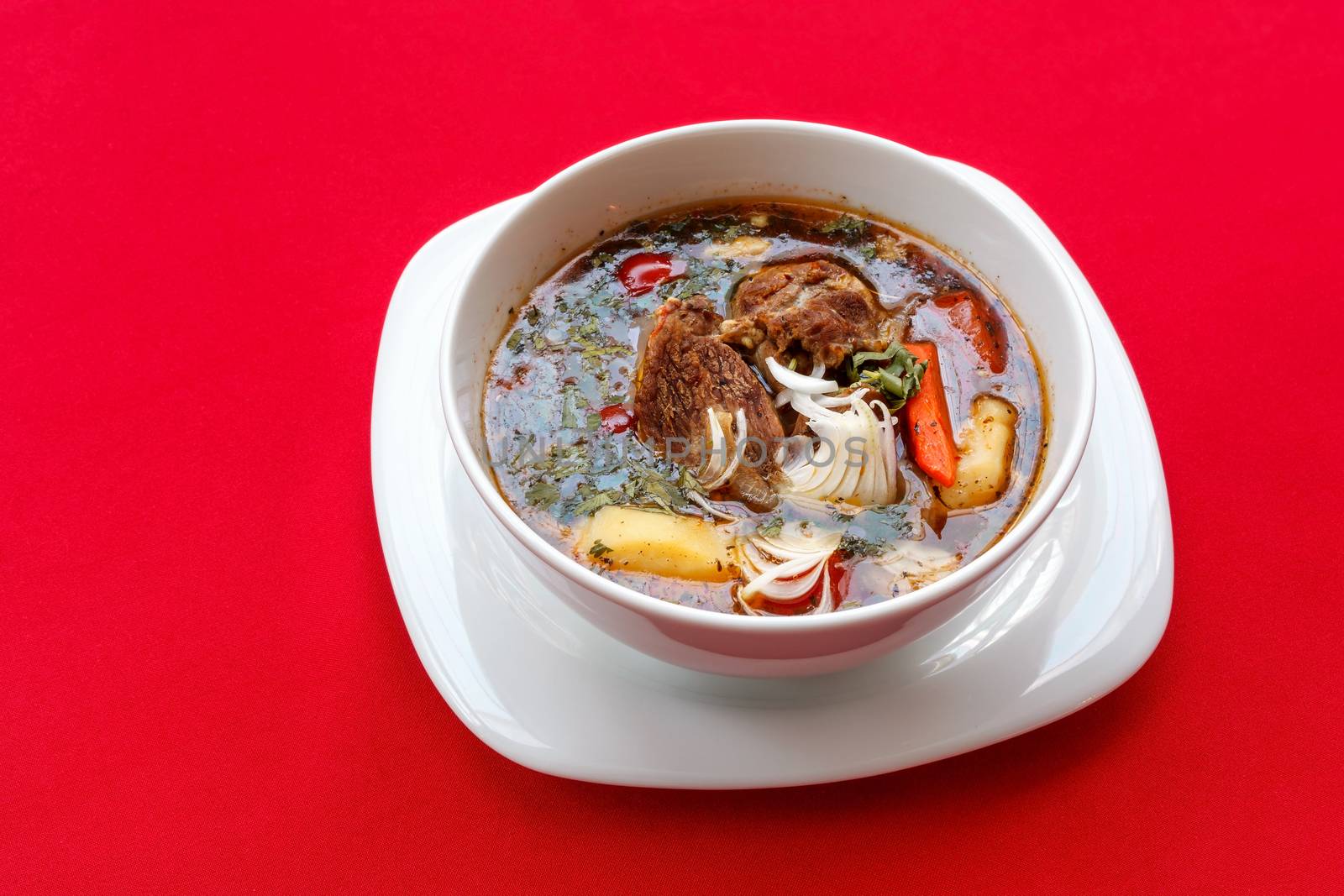 Soup with meat and sour cream on a red tablecloth. View from above close-up.