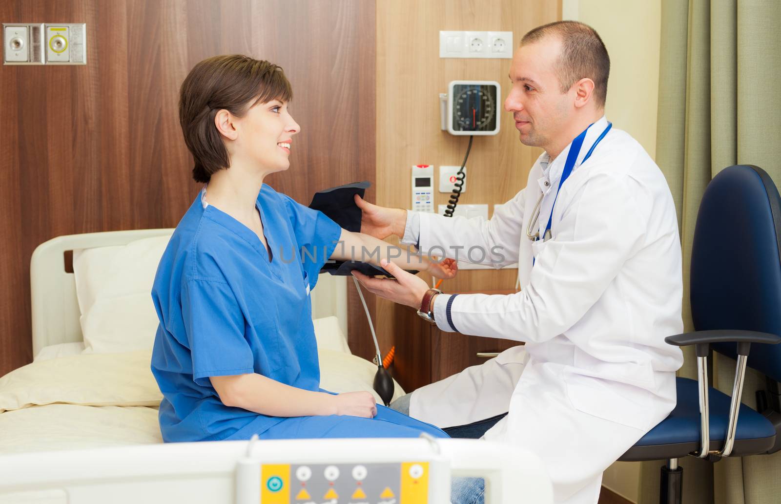 A doctor is measuring the blood pressure of a young female patient in modern hospital room.