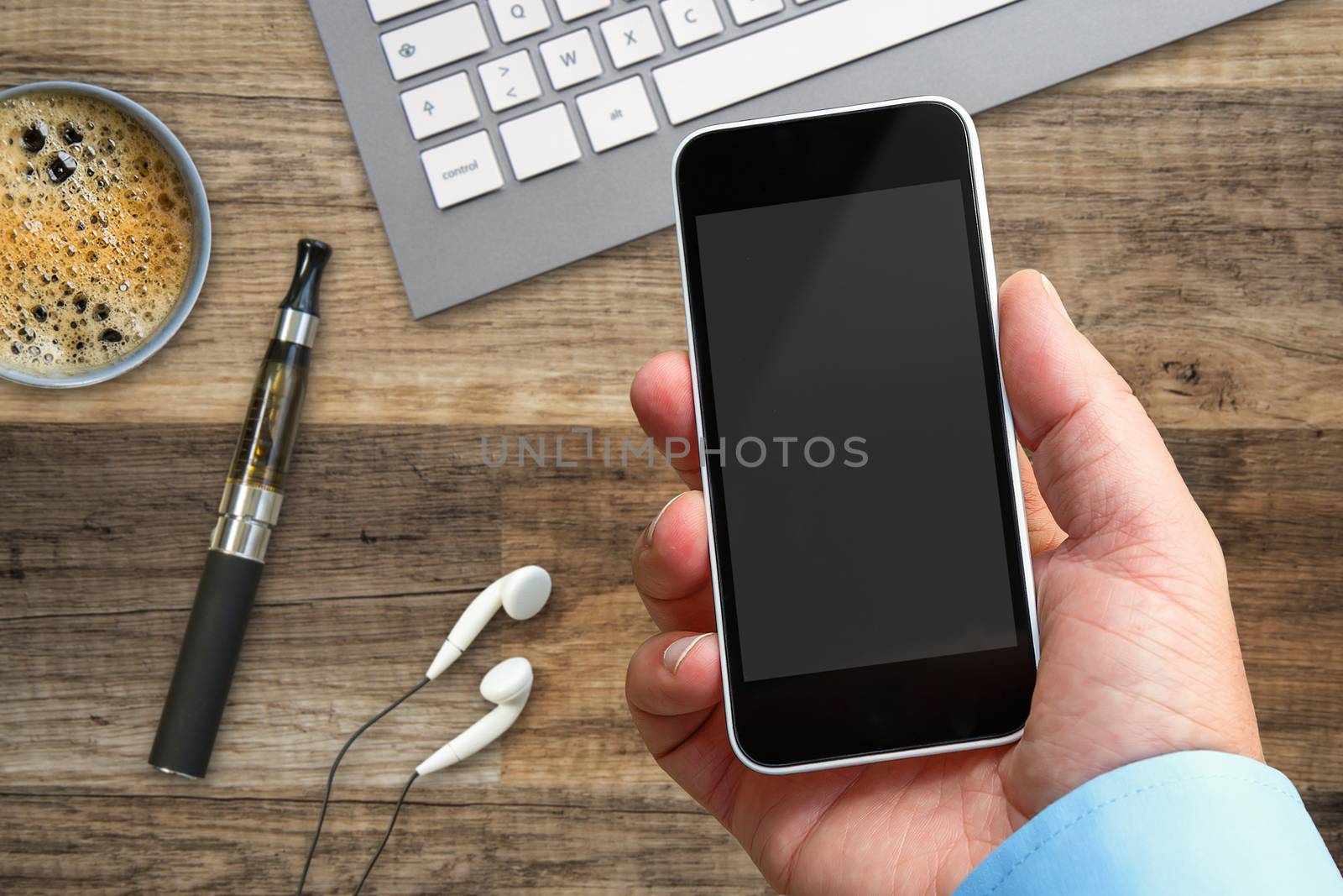 Smartphone in hand at work with a blank area to insert a custom image. Many objects placed on the wooden table by pixinoo