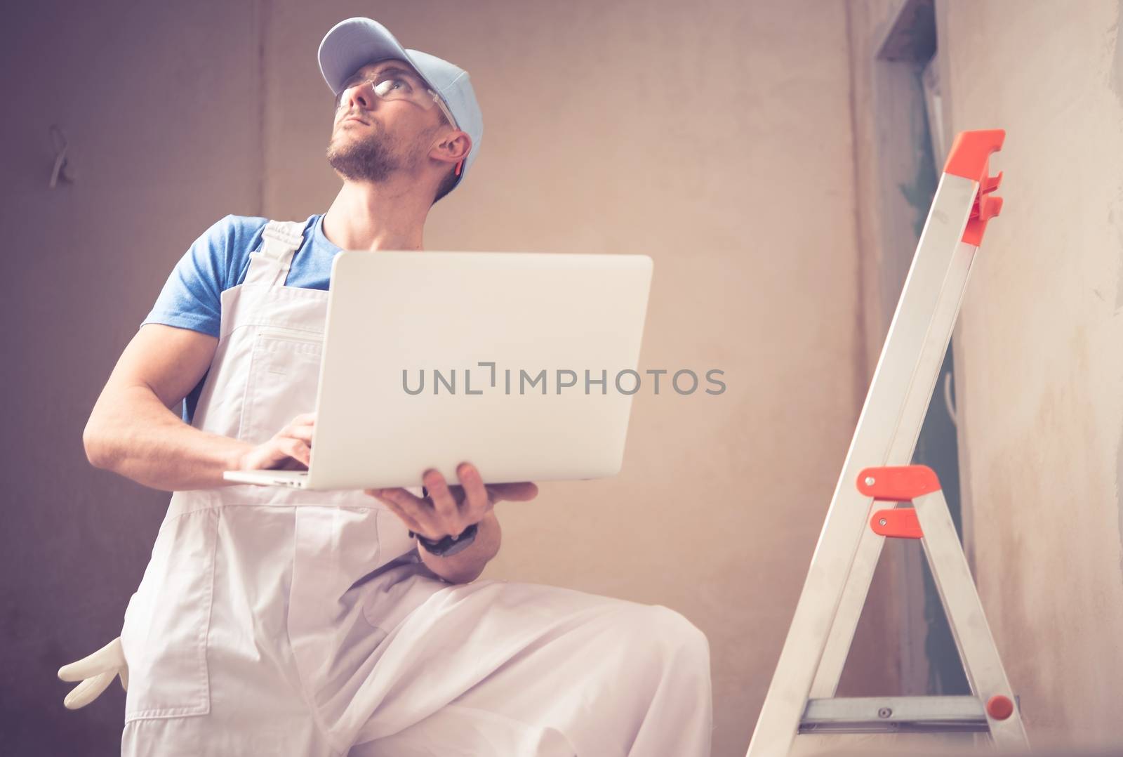Caucasian Construction Worker with Laptop Managing Remodeling Project. 
