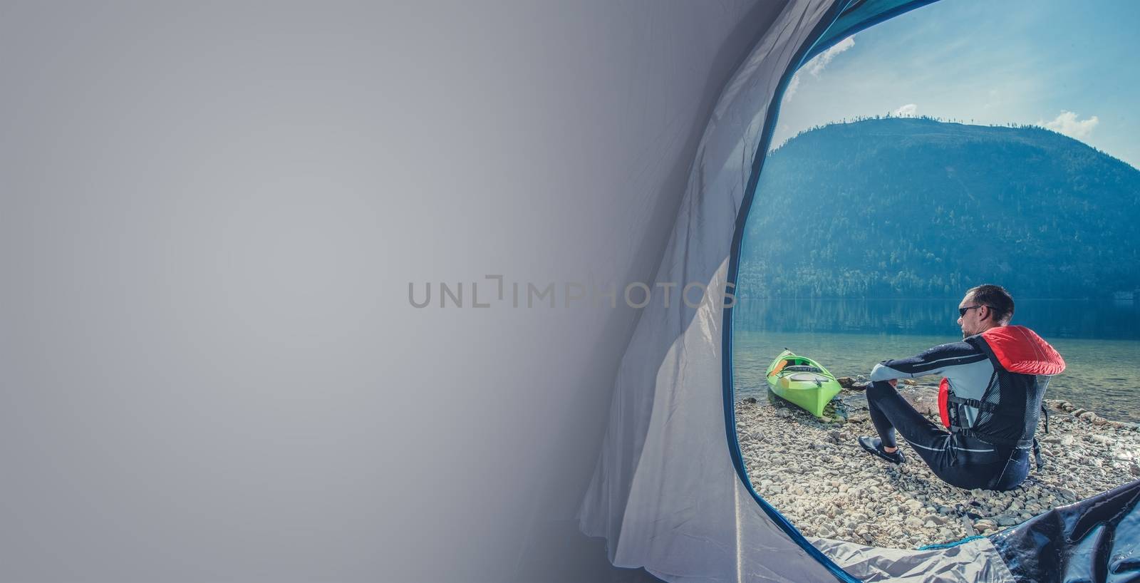 Scenic Lake Shore Camping with Kayak. Caucasian Sportsman in the Wetsuit Preparing For Kayak Trip. Photo with Copy Space.