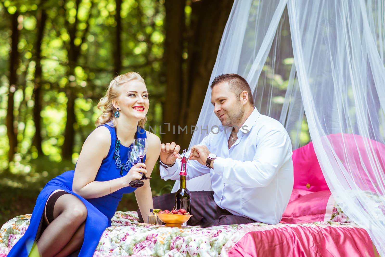 Man and woman sitting on the bed in the lawn and opening wine bottle in Lviv, Ukraine.